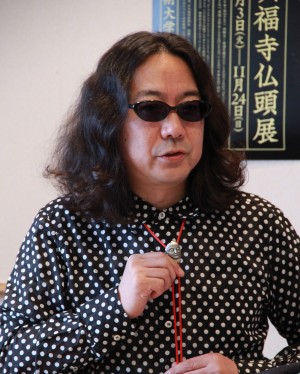 留め具が仏頭のループタイを自らつけて紹介するみうら