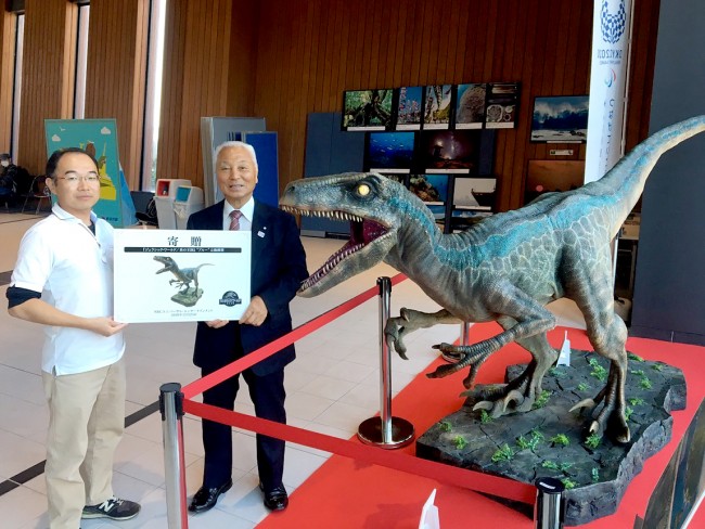 三宅島に寄贈された『ジュラシック・ワールド』恐竜“ブルー”の立像(左から、三宅村観光協会担当者、三宅村 櫻田昭正村長)